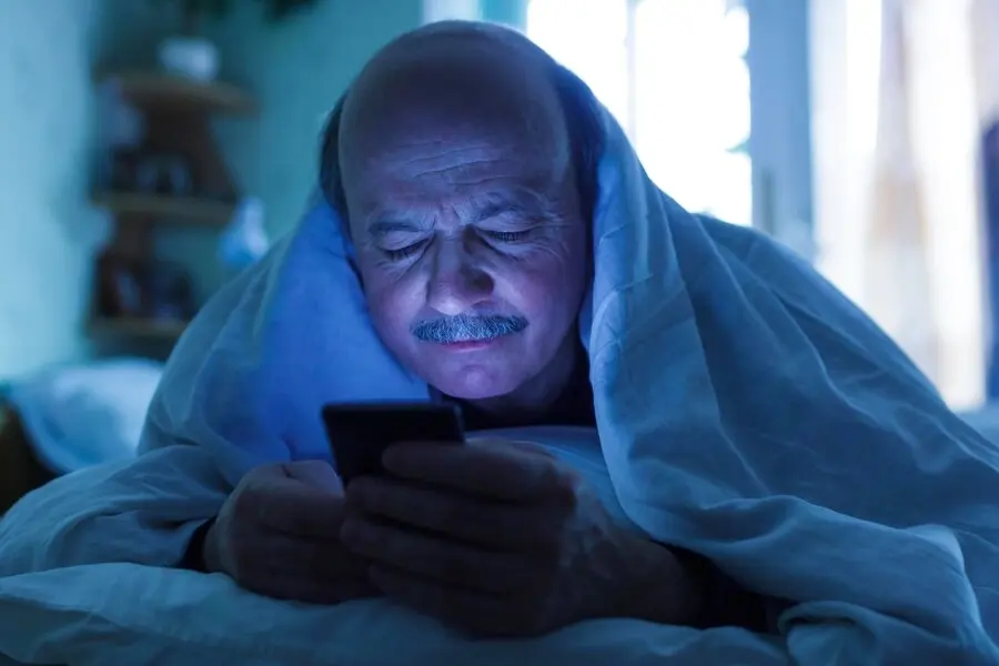 An elderly man in bed using mobile phone late at night in dark bedroom