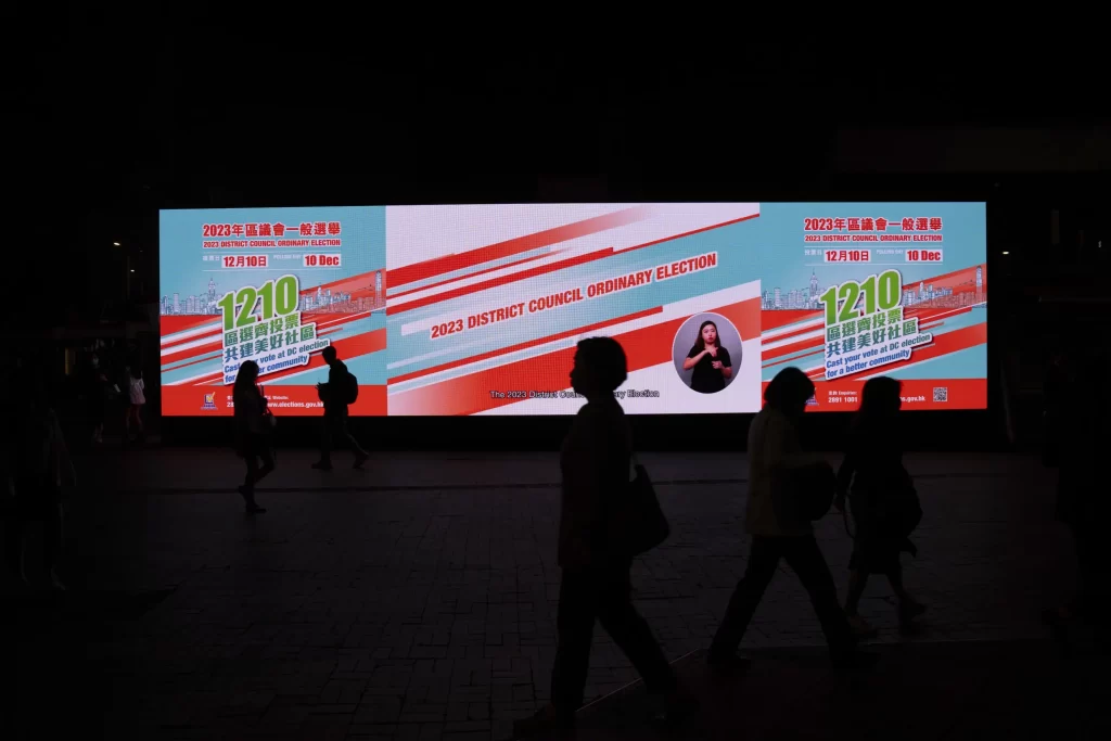 Pedestrians walk past an electronic billboard promoting the upcoming district council elections in Hong Kong