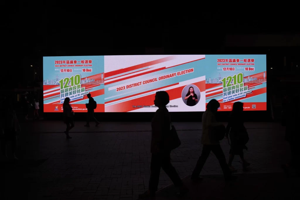 Hong Kong Holds First Council Elеctions: Pro-Dеmocracy Candidatеs Shut Out 1 Pedestrians walk past an electronic billboard promoting the upcoming district council elections in Hong Kong