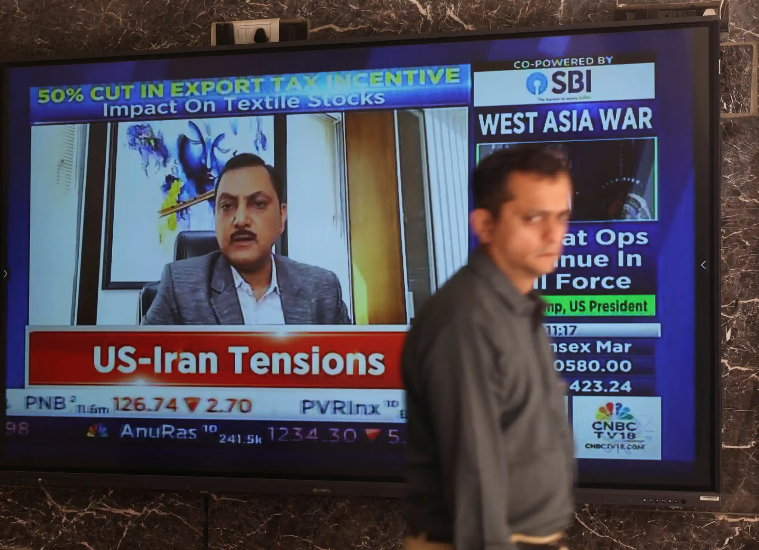 A man walks past a screen displaying the news and stock market updates at the Bombay Stock Exchange (BSE) in Mumbai, India, March 2, 2026. REUTERS/Francis Mascarenha