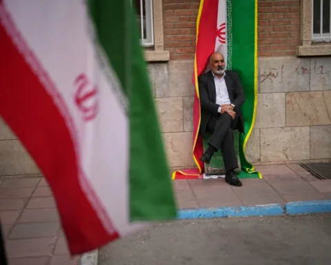 A man sits beside an Iranian flag banner during a government-sponsored protest attended by medical workers against the U.S.-Israeli military campaign outside Imam Khomeini Hospital in Tehran, Iran, Monday, April 6, 2026. (Photo: AP)